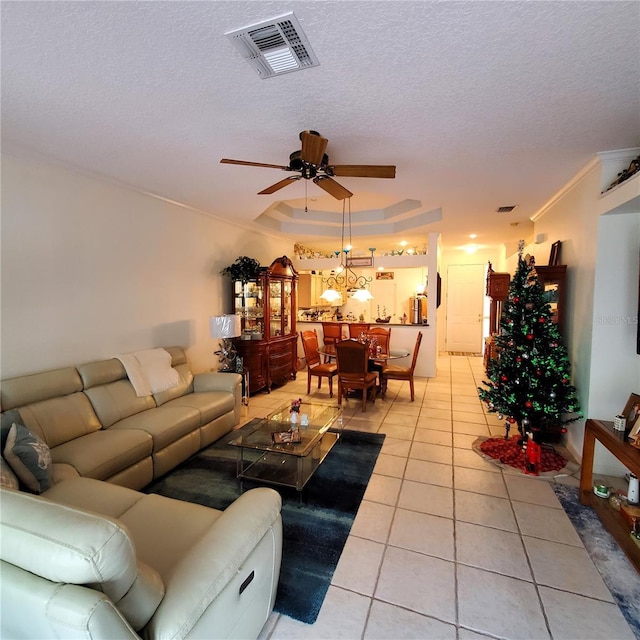 tiled living room featuring a textured ceiling, a raised ceiling, ceiling fan, and ornamental molding