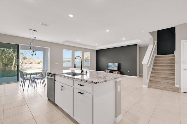 kitchen featuring a raised ceiling, sink, a center island with sink, white cabinets, and hanging light fixtures