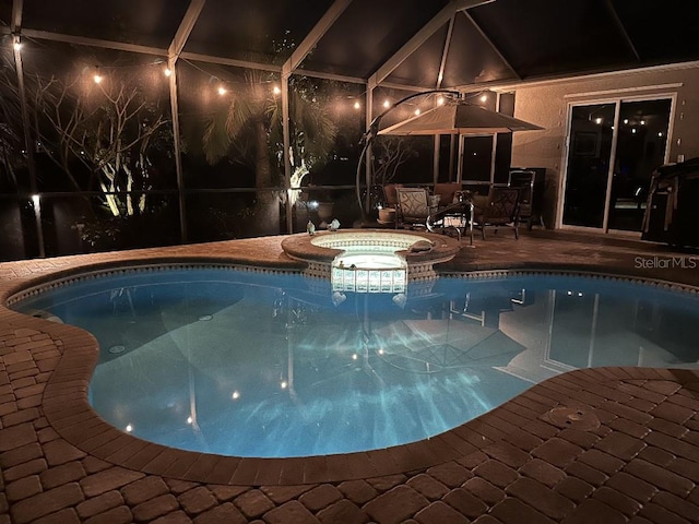 pool at twilight featuring glass enclosure, a patio area, and an in ground hot tub