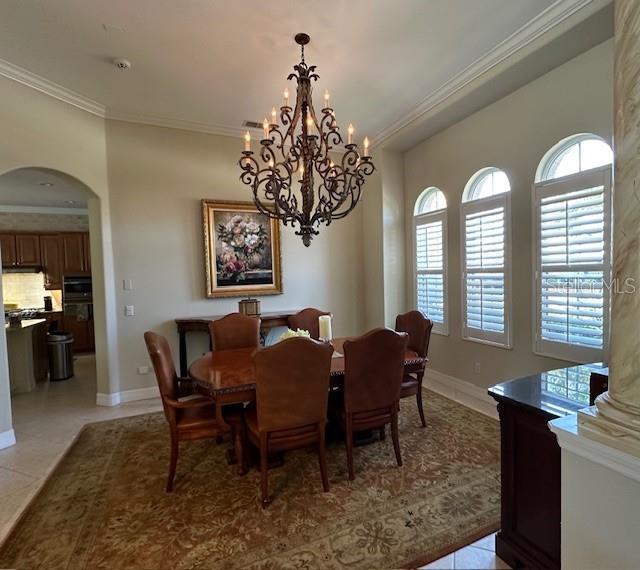 dining area featuring arched walkways, a chandelier, baseboards, light tile patterned floors, and ornamental molding