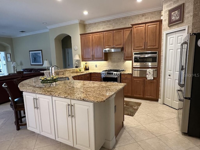 kitchen featuring appliances with stainless steel finishes, a sink, arched walkways, under cabinet range hood, and a warming drawer