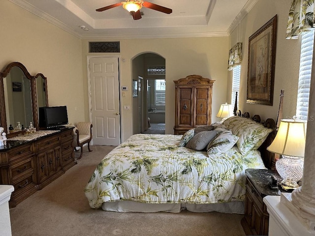 carpeted bedroom with arched walkways, a tray ceiling, and ornamental molding