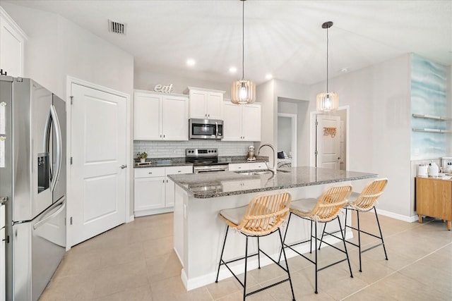 kitchen featuring dark stone countertops, pendant lighting, a kitchen island with sink, white cabinets, and appliances with stainless steel finishes