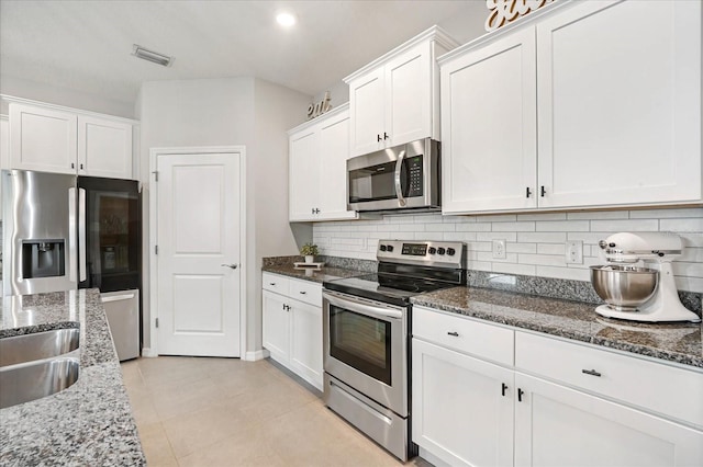 kitchen with dark stone countertops, decorative backsplash, white cabinets, and stainless steel appliances