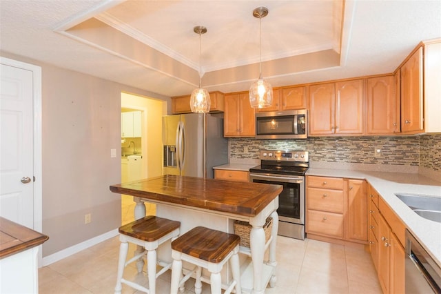 kitchen featuring hanging light fixtures, decorative backsplash, a tray ceiling, light tile patterned flooring, and stainless steel appliances