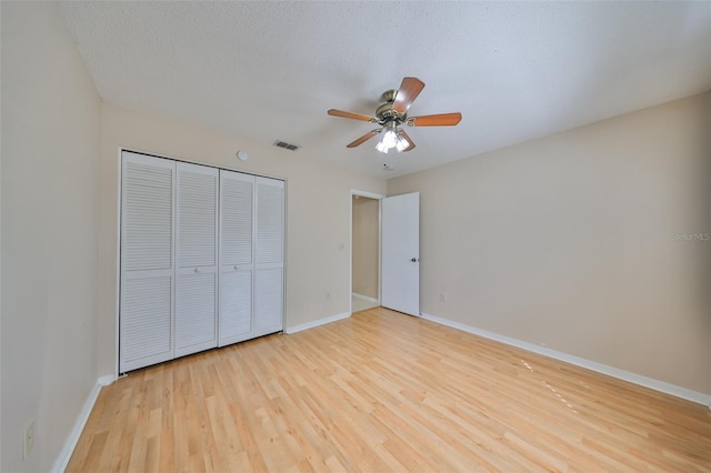 unfurnished bedroom with a textured ceiling, a closet, light hardwood / wood-style flooring, and ceiling fan