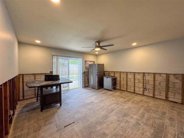 kitchen featuring a textured ceiling, stainless steel fridge, ceiling fan, and wood walls