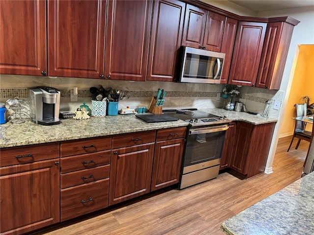 kitchen with backsplash, light stone countertops, stainless steel appliances, and light wood-type flooring