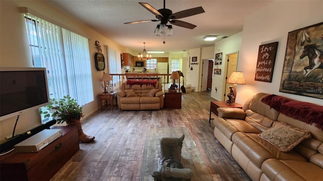 living room with a wealth of natural light, dark wood-type flooring, a textured ceiling, and ceiling fan with notable chandelier