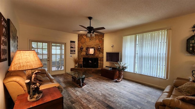 living room featuring ceiling fan, a stone fireplace, dark wood-type flooring, and a textured ceiling