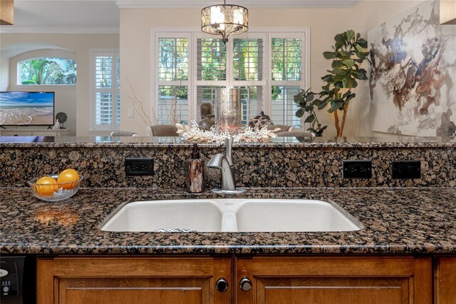 details featuring pendant lighting, dark stone counters, an inviting chandelier, sink, and ornamental molding