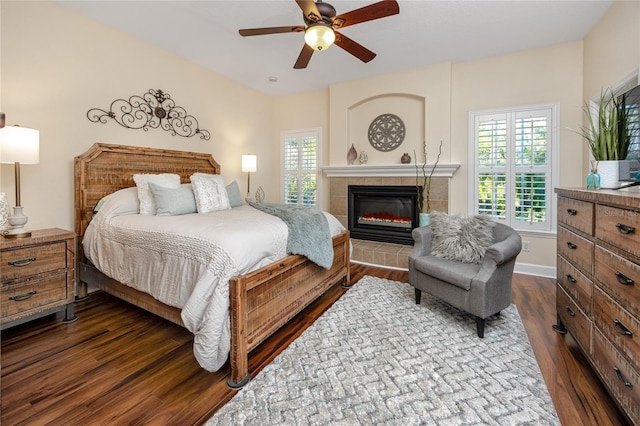 bedroom featuring hardwood / wood-style floors, ceiling fan, and a tiled fireplace