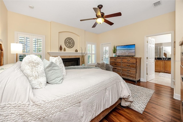 bedroom featuring connected bathroom, ceiling fan, dark hardwood / wood-style flooring, and a tile fireplace