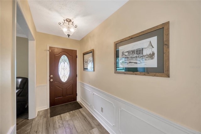 entryway with wood-type flooring, a textured ceiling, and a notable chandelier