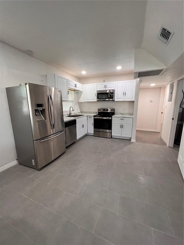 kitchen with lofted ceiling, sink, light tile patterned floors, appliances with stainless steel finishes, and white cabinetry