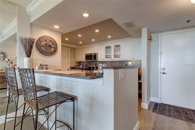 kitchen featuring a breakfast bar, white cabinets, kitchen peninsula, stainless steel appliances, and light hardwood / wood-style flooring