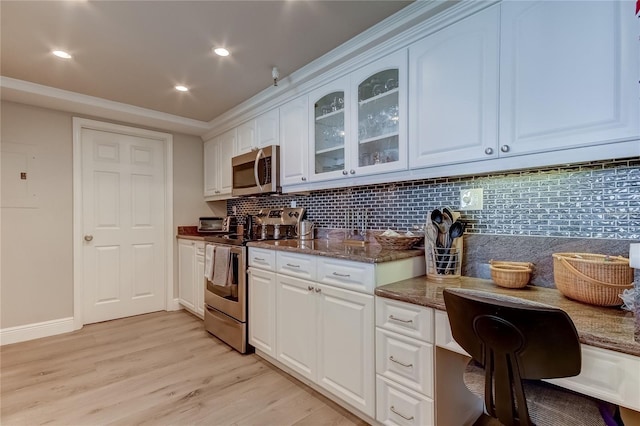 kitchen featuring tasteful backsplash, white cabinets, dark stone counters, stainless steel appliances, and light wood-type flooring