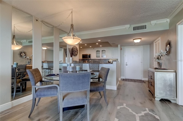 dining room featuring ornamental molding, a textured ceiling, and light wood-type flooring