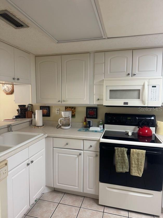 kitchen featuring white cabinets, light tile patterned floors, white appliances, and sink