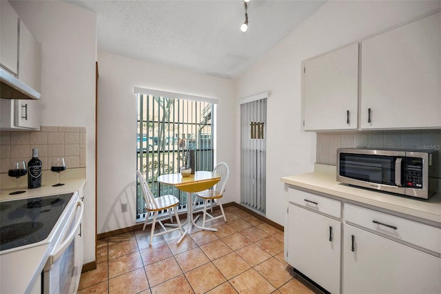 kitchen with stove, lofted ceiling, backsplash, white cabinets, and light tile patterned floors