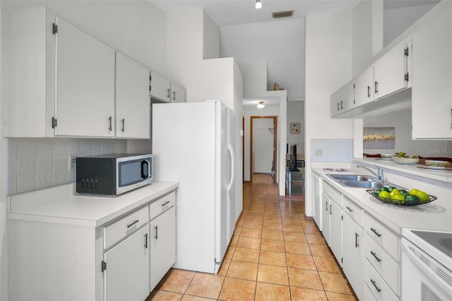 kitchen with stove, sink, light tile patterned floors, white fridge, and white cabinetry