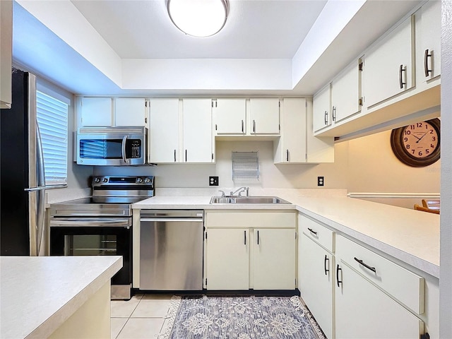 kitchen featuring appliances with stainless steel finishes, a tray ceiling, sink, white cabinets, and light tile patterned flooring