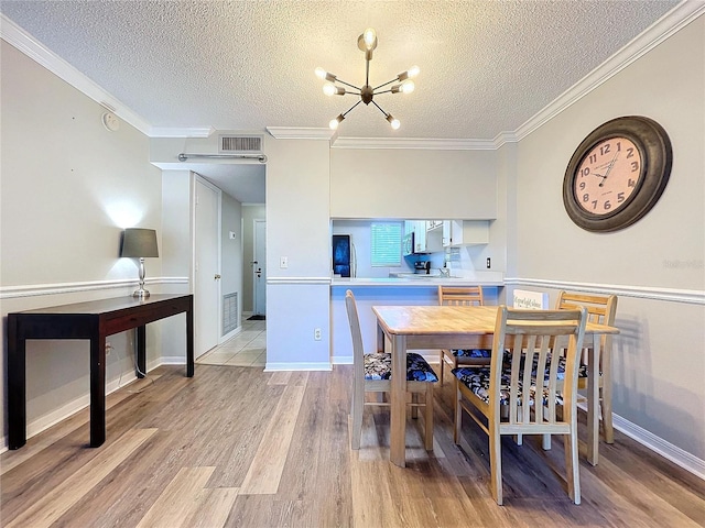 dining area featuring a notable chandelier, light wood-type flooring, ornamental molding, and a textured ceiling