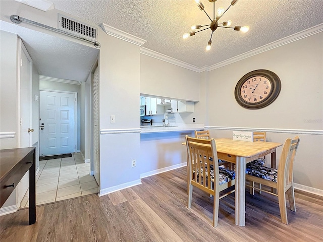 dining room with an inviting chandelier, sink, crown molding, a textured ceiling, and light hardwood / wood-style floors