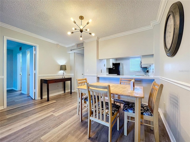 dining room featuring sink, a notable chandelier, hardwood / wood-style floors, a textured ceiling, and ornamental molding