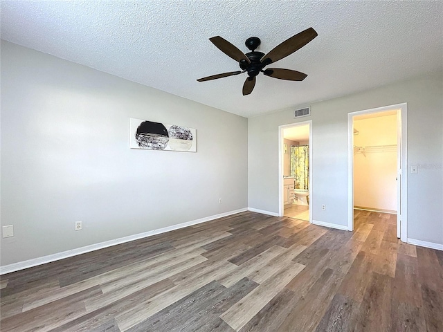 unfurnished bedroom featuring a walk in closet, hardwood / wood-style flooring, ceiling fan, a textured ceiling, and a closet