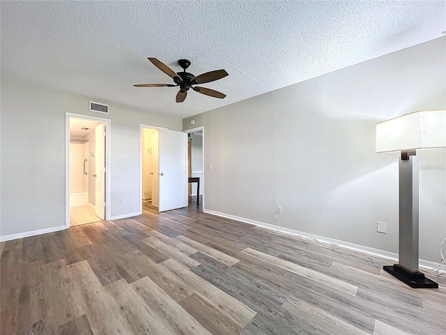 unfurnished bedroom with a textured ceiling, light wood-type flooring, ensuite bathroom, and ceiling fan