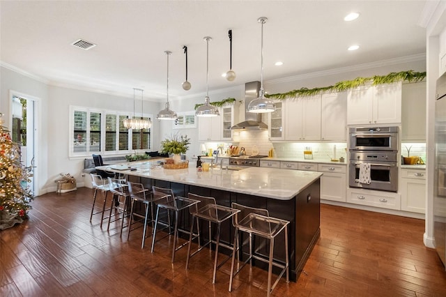 kitchen featuring a large island with sink, a breakfast bar, wall chimney exhaust hood, and appliances with stainless steel finishes