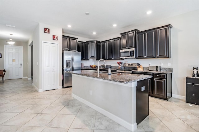 kitchen featuring sink, stainless steel appliances, dark stone countertops, a center island with sink, and light tile patterned flooring