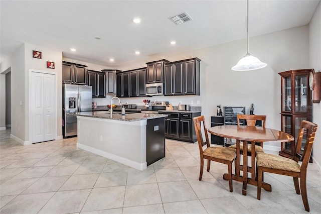 kitchen featuring a kitchen island with sink, decorative light fixtures, light tile patterned floors, appliances with stainless steel finishes, and stone countertops