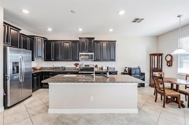 kitchen featuring stainless steel appliances, a kitchen island with sink, sink, decorative light fixtures, and stone countertops