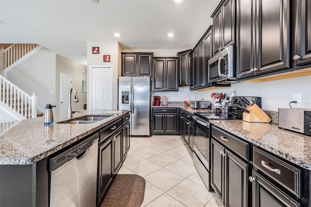 kitchen with appliances with stainless steel finishes, light stone counters, sink, an island with sink, and light tile patterned flooring