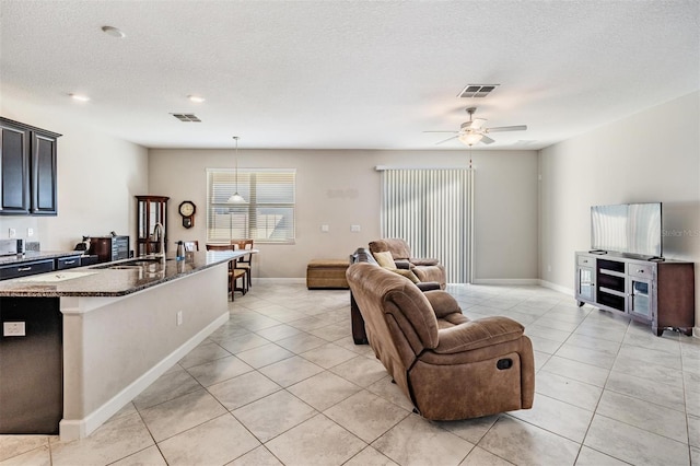 living room featuring ceiling fan, light tile patterned flooring, sink, and a textured ceiling