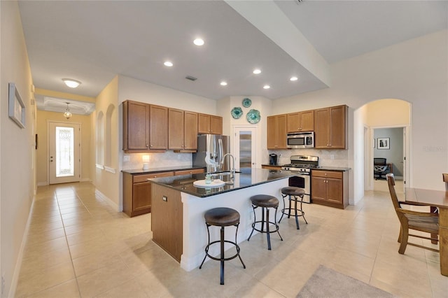 kitchen with a kitchen island with sink, stainless steel appliances, decorative backsplash, a breakfast bar, and light tile patterned floors