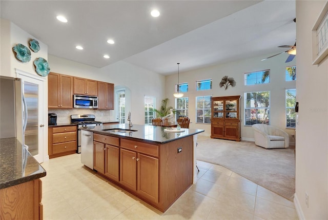 kitchen with sink, hanging light fixtures, stainless steel appliances, light carpet, and a center island with sink