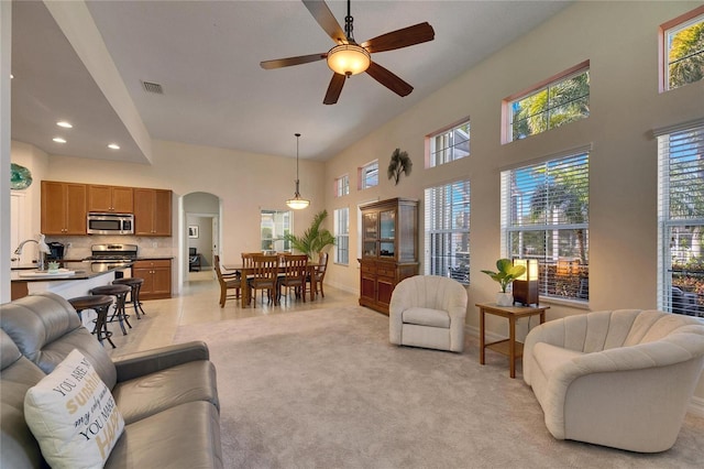 living room with ceiling fan, sink, light colored carpet, and a high ceiling