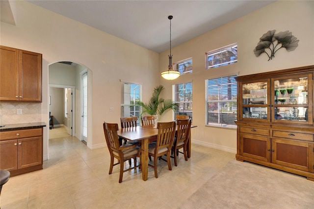 dining room with light tile patterned flooring, baseboards, arched walkways, and a towering ceiling