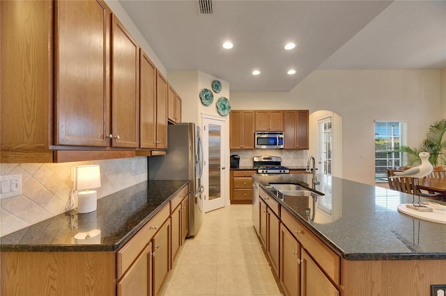 kitchen with backsplash, dark stone counters, stainless steel appliances, sink, and an island with sink