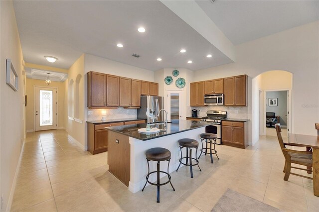 kitchen with a kitchen bar, arched walkways, dark countertops, and appliances with stainless steel finishes