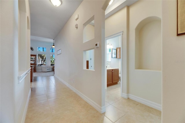 hall with light tile patterned floors, baseboards, and a towering ceiling