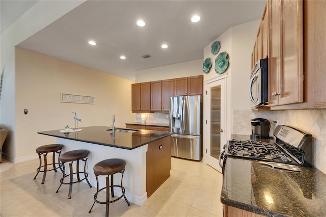 kitchen featuring a center island with sink, a breakfast bar, brown cabinetry, stainless steel appliances, and a sink