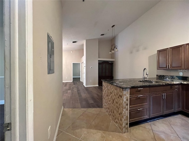 kitchen featuring kitchen peninsula, light tile patterned floors, dark stone countertops, and sink