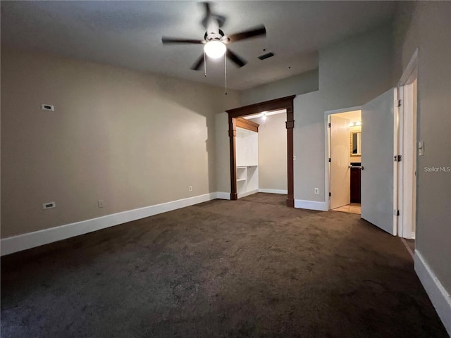 unfurnished bedroom featuring dark colored carpet, ensuite bathroom, ceiling fan, a spacious closet, and a closet