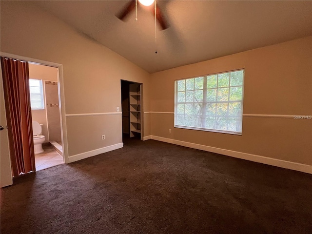 unfurnished bedroom featuring ensuite bath, ceiling fan, lofted ceiling, and dark colored carpet