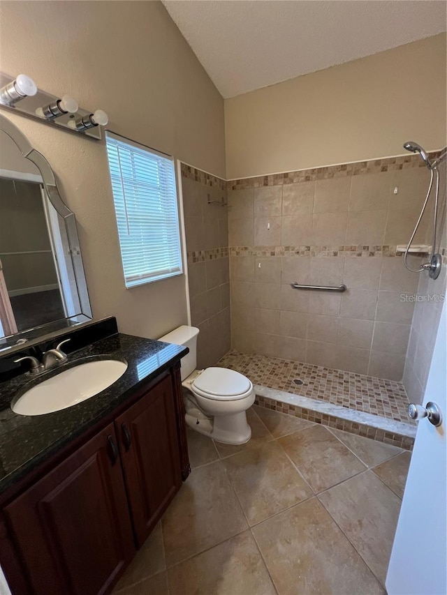 bathroom featuring tile patterned floors, vanity, vaulted ceiling, tiled shower, and toilet