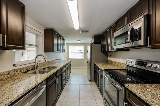 kitchen featuring appliances with stainless steel finishes, light stone counters, dark brown cabinetry, sink, and light tile patterned floors